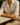 Woman sitting at a table wearing a white shirt and beige pants, with a blurred background.